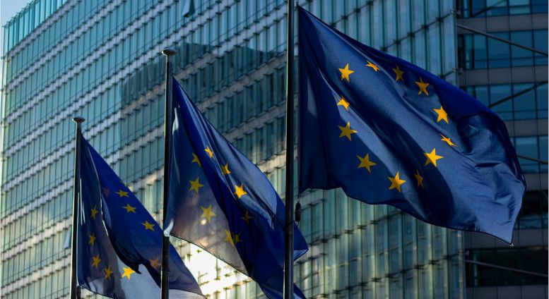 Drei Flaggen der EU vor einem Gebäude aus Glas.